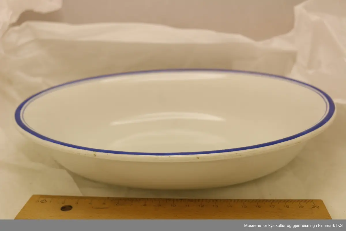 En avlang rund matserveringsskål av glasert keramikk. Produsert av Egersund Fayancefabriks Co. Skålen er hvit med blå striper langs skålkanten