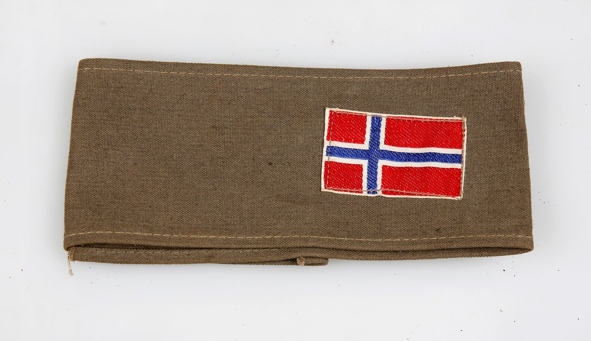 Avlang remse av militærgrønn lerret med norsk flagg. Feste sammen med svart sikkerhetsnål.