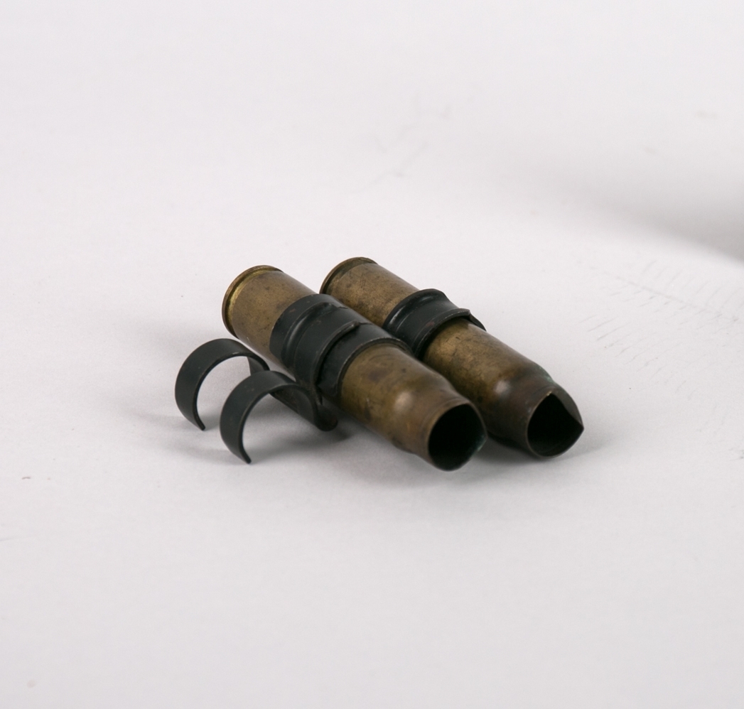 Patronhylse. To ammunisjonhylser fra det britiske flyangrepet på MS SIRIUS som ble senket 9. januar 1945 i Fuglesetfjorden, Bjordal i Sognefjorden. Hylsene ca. 20 mm (uten ammunisjon) er koblet sammen med sort beslag .