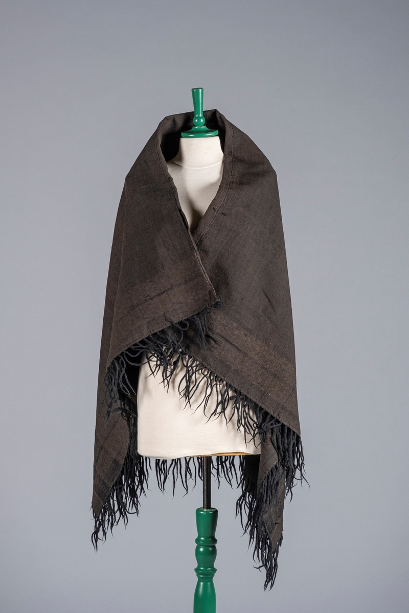 Sort sjal sydd sammen av to deler. Det er frynser i kantene. Sjalet har mønster av to brede striper langs kantene.