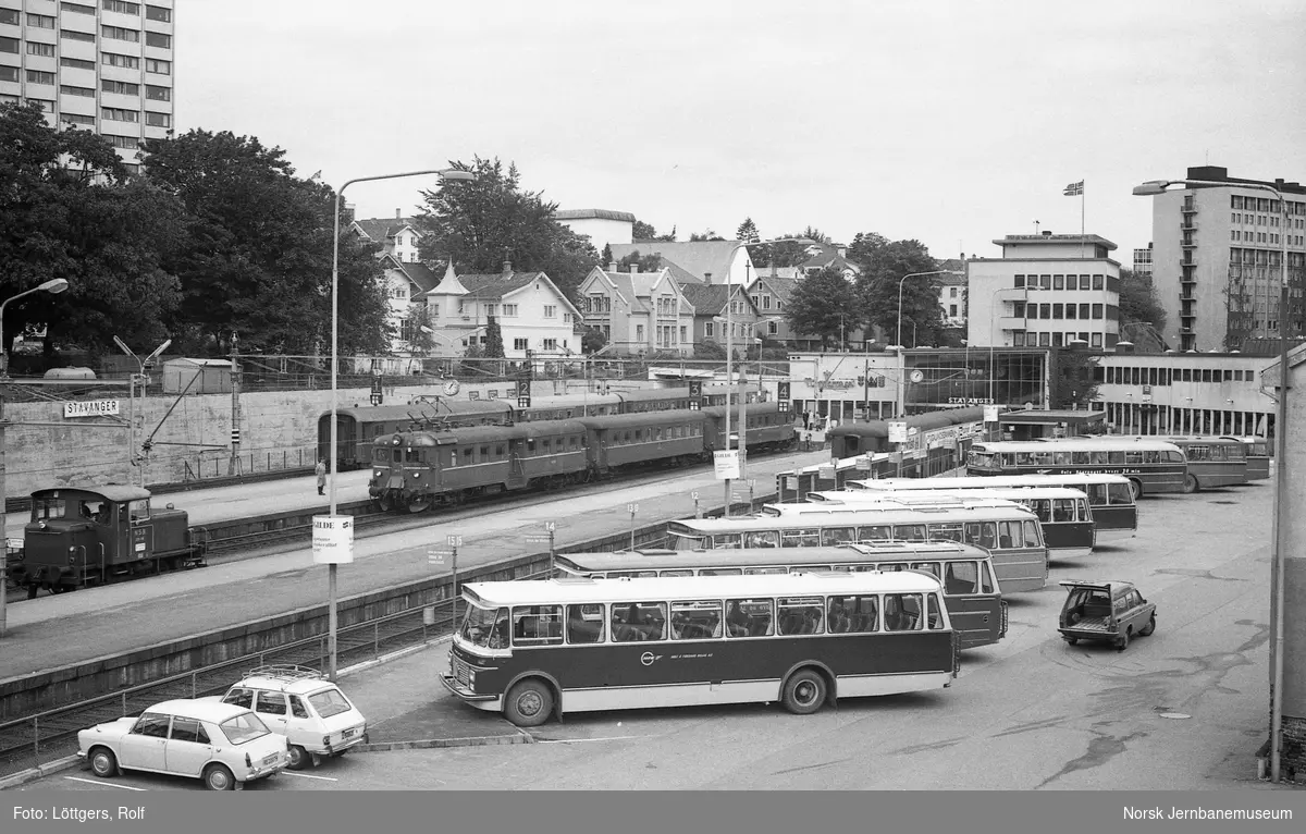 Stavanger jernbanestasjon og rutebilstasjon. I forgrunnen diverse rutebusser. I bakgrunnen, nærmest elektrisk motorvognsett type 68A, i bakgrunnen personvognene til ettermiddagsekspressen til Oslo V, tog 74.