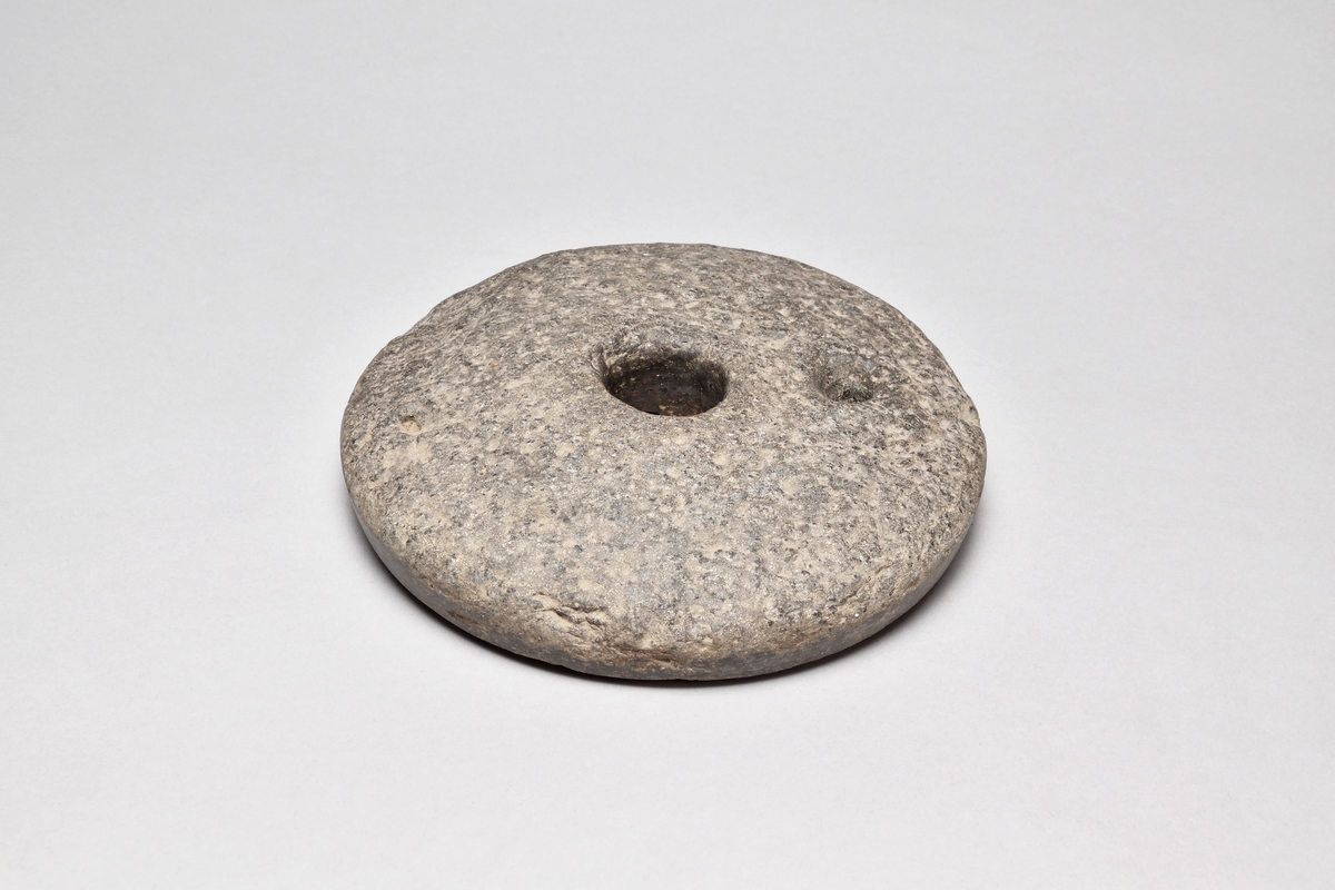 Snuskvarn av sten, rund, i två delar. Överliggaren med två hål, det ena för draghandtag. Underliggaren med ett hål.