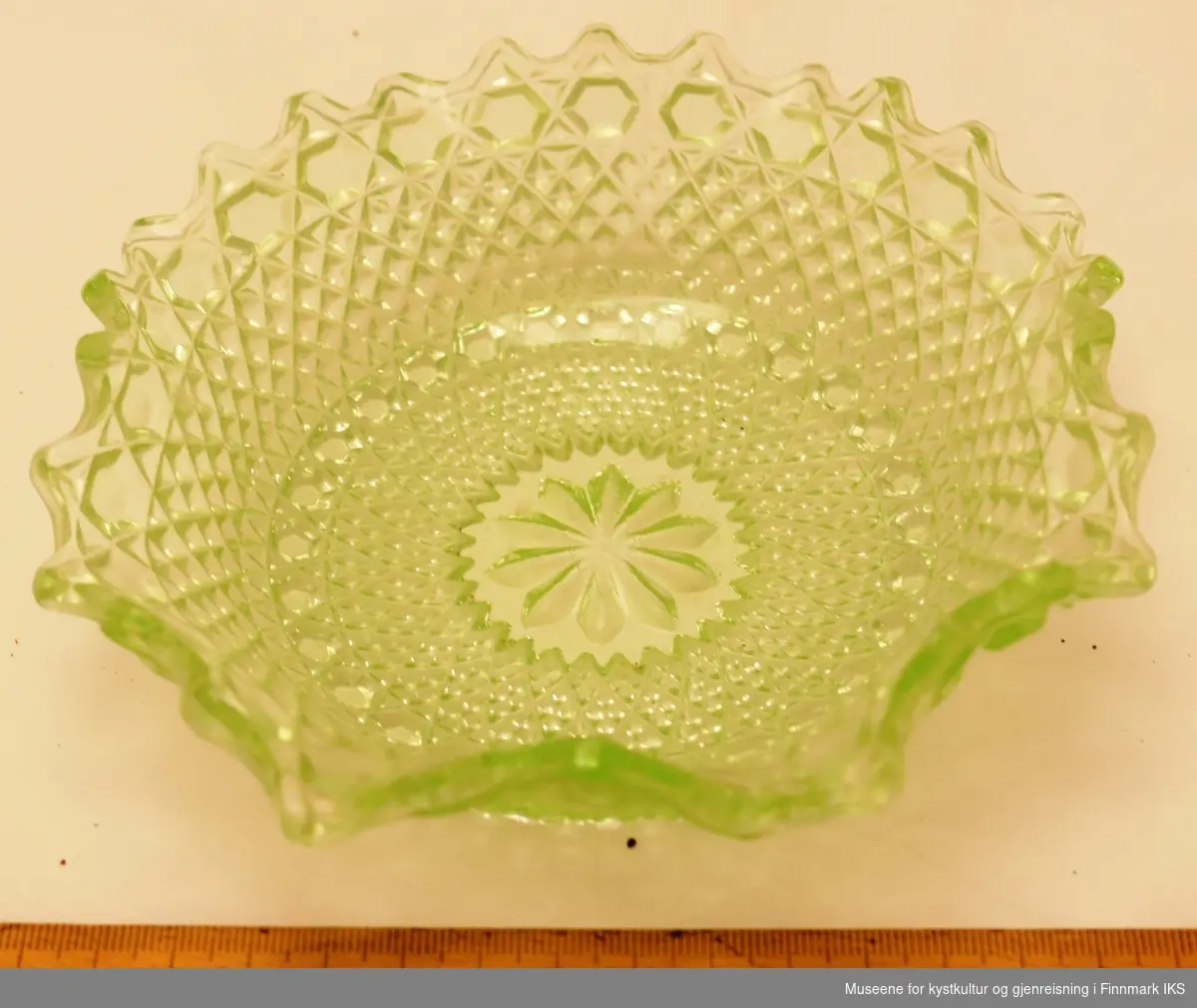 En grønn glasskål med presset mønster på utsiden og buede kanter