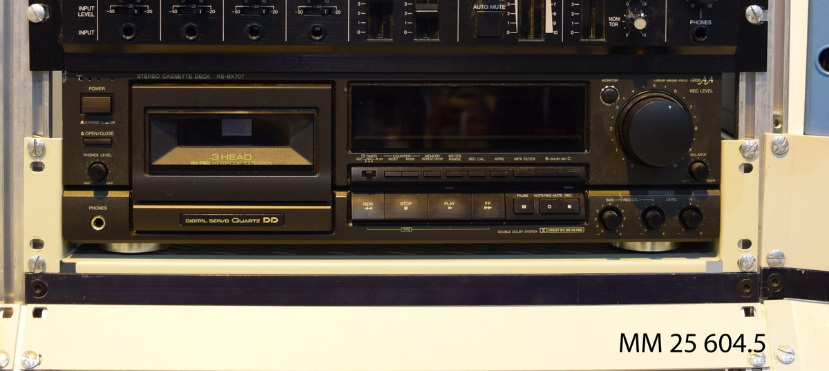 Kassettbandspelare av märket Technics – RS-BX 707. 2-kanals. Svart rektangulär apparat, plats för en kassett samt diverse rattar och knappar för inställningar och funktioner.