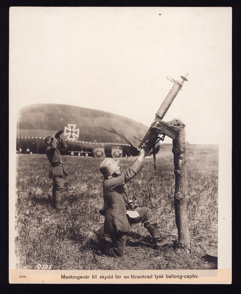 Bilden visar en soldater som siktar mot himmelen med kulspruta, som är fastmonterad på en avsågat trädstam.  I bakgrunden ser man en spaningsballong liggande på marken.