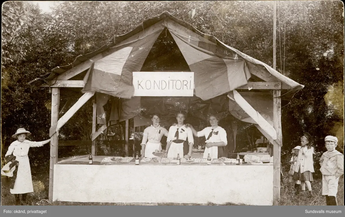 Vykort med motiv av ett marknadsstånd med skylten konditori. Enligt texten på baksidan: Wärstaparken 26 juli 1914.