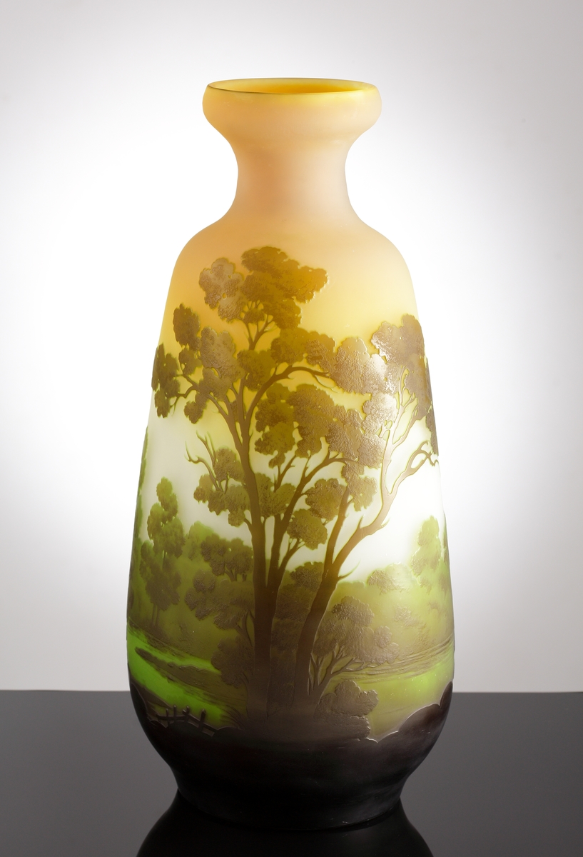 Opak vas som skiftar från orange, till gult, till vitt. Etsat överfång i gröna nyanser som avslutas i svart ner mot vasens botten. Motivet är ett sommarlandskap med en sjö och omgivande träd.