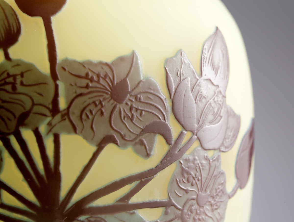 Halvopak, gulvit vas med etsat överfång i blålila nyanser som avslutas i en mörk fot. Sjöväxter med bl. a näckrosor är avbildade som dekor.
