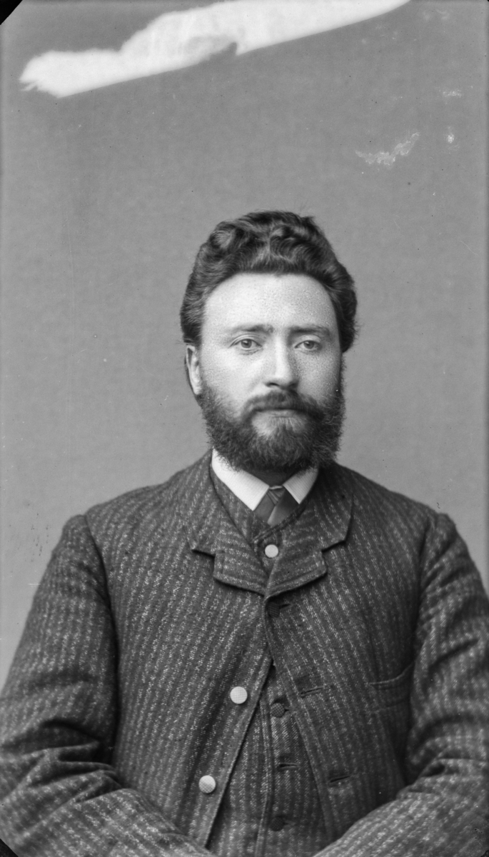Portrett av mann med mørkt hår, bart og sjegg, kledd i kvit sjorte, slips og stripet vest og jakke