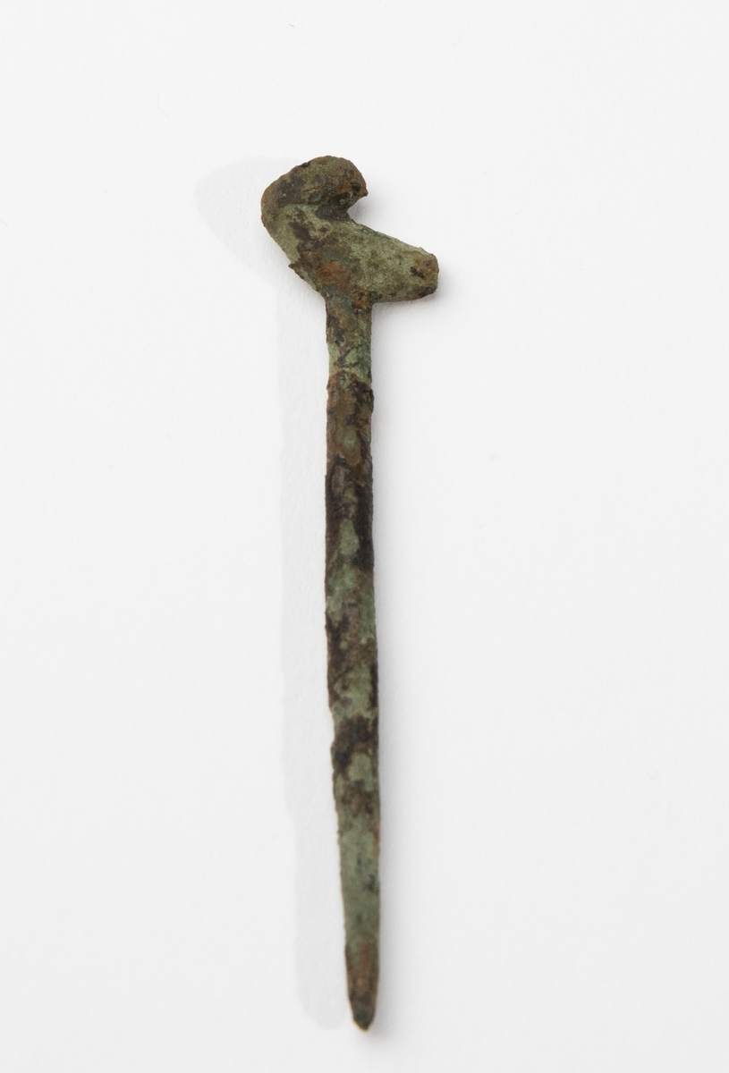 Dräktnål av brons med C-format huvud. Påträffad i grav A25. Nålen liknar vagt så kallade fågelnålar, men denna saknar i så fall huvudet.