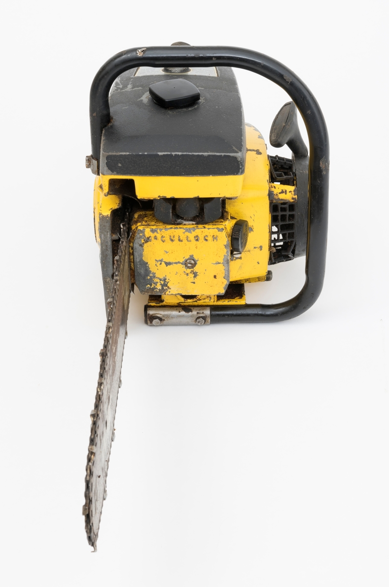 En McCulloch CP 70 motorsag, gul med svart startsnorhåndtak, gasshendel, choke, struper, lydpotte. Instruksjon på toppdekselet. Motprsaga har påmontert sverd og sagkjede (skovltannkjede).