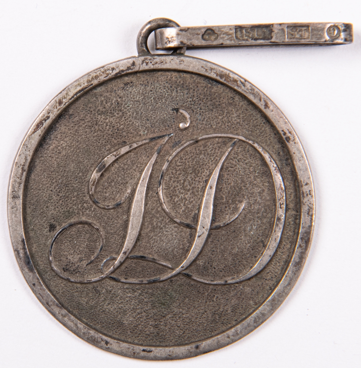 Emblem för föreningen Idka Dygden. Rund form med hänge.
Del av 6 stycken föreningestecken i silver, två korsformiga, 4 runda.