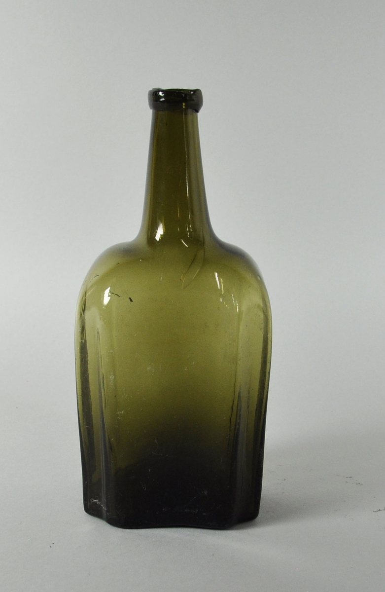 Åttekantet grønn flaske av glass med lang hals.