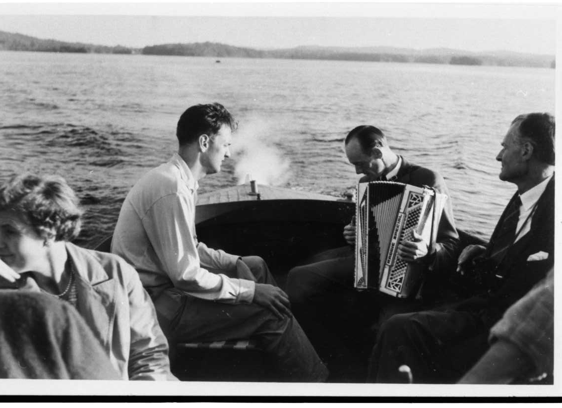 En utflykt med båt på sjön Bunn. I aktern sitter Rolf von Otter och tittar mot Gunnar Edén som sitter mittemot och spelar dragspel. Hitom dem sitter en okänd man och kvinna.