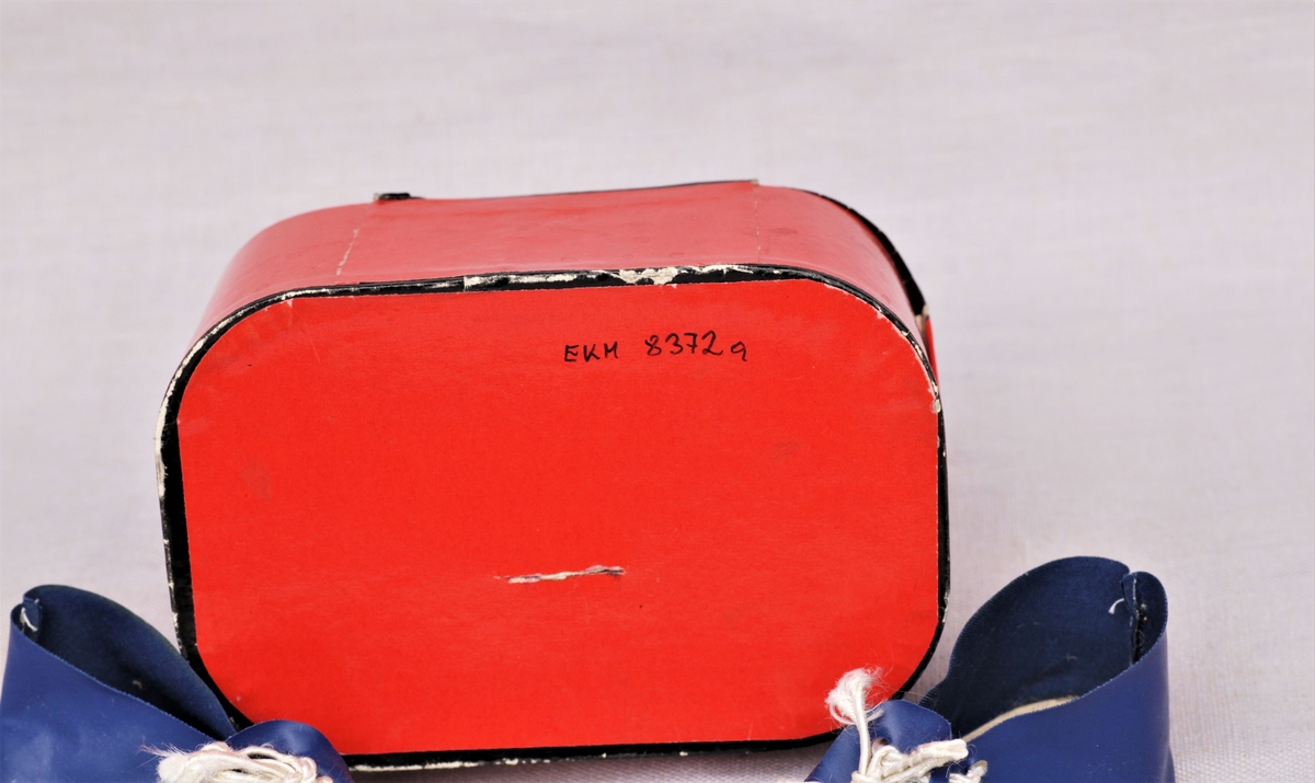 Rød koffert med trykknapp og svart kant, og et par blå dukkesko med hvite lisser.