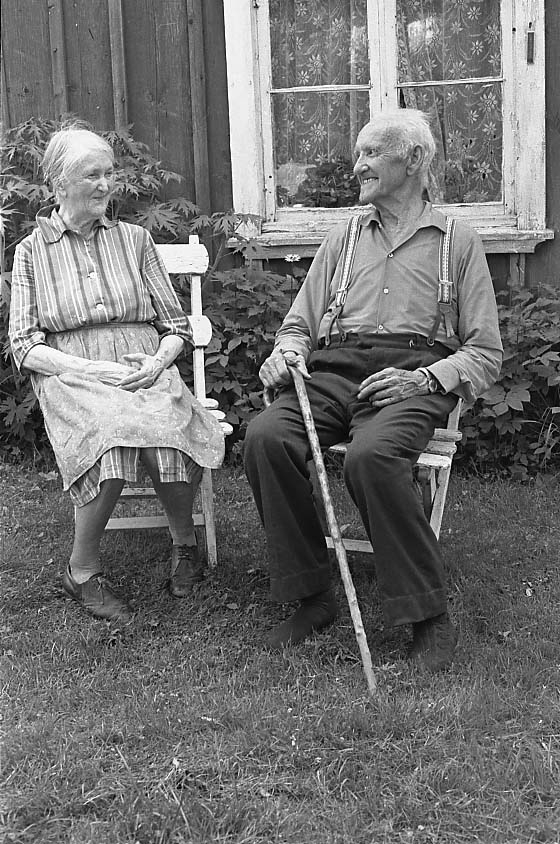 På gräsmattan framför huset i Vässingarp sitter en äldre man, Karl Fransson, i en trädgårdsstol Han är klädd i skjorta och byxor med hängslen och strumpor utan skor. Han håller en käpp i höger hand. Till vänster sitter han hushållerska, en äldre kvinna vid namn Helga Carlsson. Hon bär en randig klänning med förkläde. De sitter vända mot varandra och skrattar.