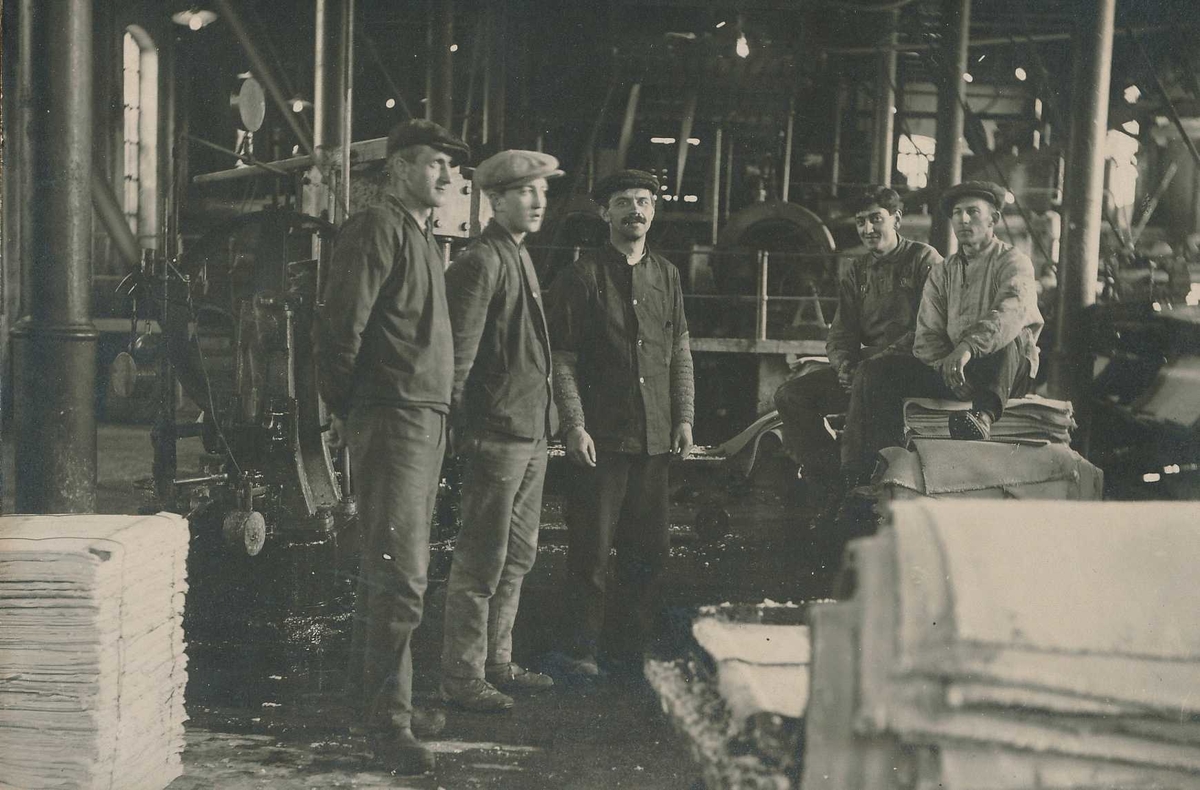 Fem arbeidere i arbeidsantrekk inne i produksjonssalen i det gamle tresliperiet på Kistefoss