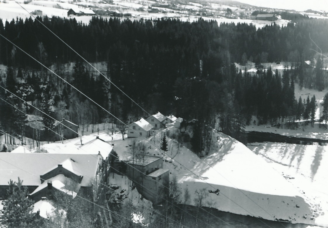 Fabrikkområde med to tresliperi, kraftstasjon og arbeiderboliger fotografert om vinteren. I bakgrunnen er det skog og jordbrukslandskap.