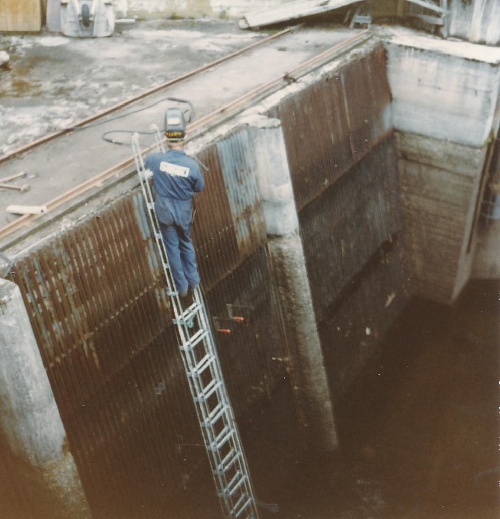 Mann står på stige og holder på med reparasjoner av varegrind på Kistefoss
