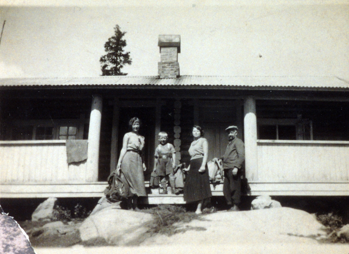 To kvinner, en mann og en gutt på trappen foran en hytteveranda. Alle holder på ryggsekker.