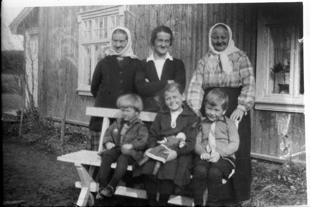 Avfotografert portrett av tre eldre kvinner som står bak en krakk foran en husvegg, og tre barn som sitter på krakken. Kvinnen i midten bak er Åsta Hansen, gift med Markus. Barna antas å være hennes tre eldste barn, fra venstre Magne, Aase og Bjørn. De to eldre damene er ukjente,