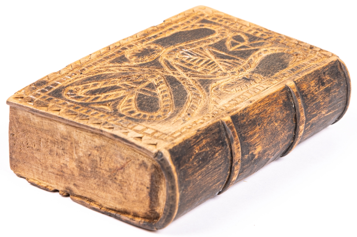 Ask, av trä, i form av bok, med ena pärmen som skjutlock. Prydd med ristade ornament.
Kan ha använts för tobak.