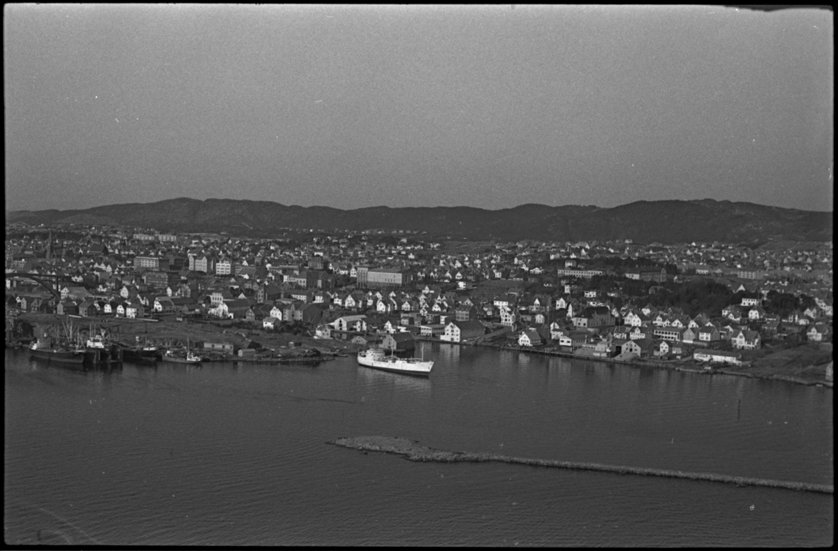 Haugesund Mekaniske Verksted sett fra vest. Det er skip i produksjon både i tørrdokken og i flytedokken og flere skip ligger til kai. Haugesund ligger i bakgrunnen.