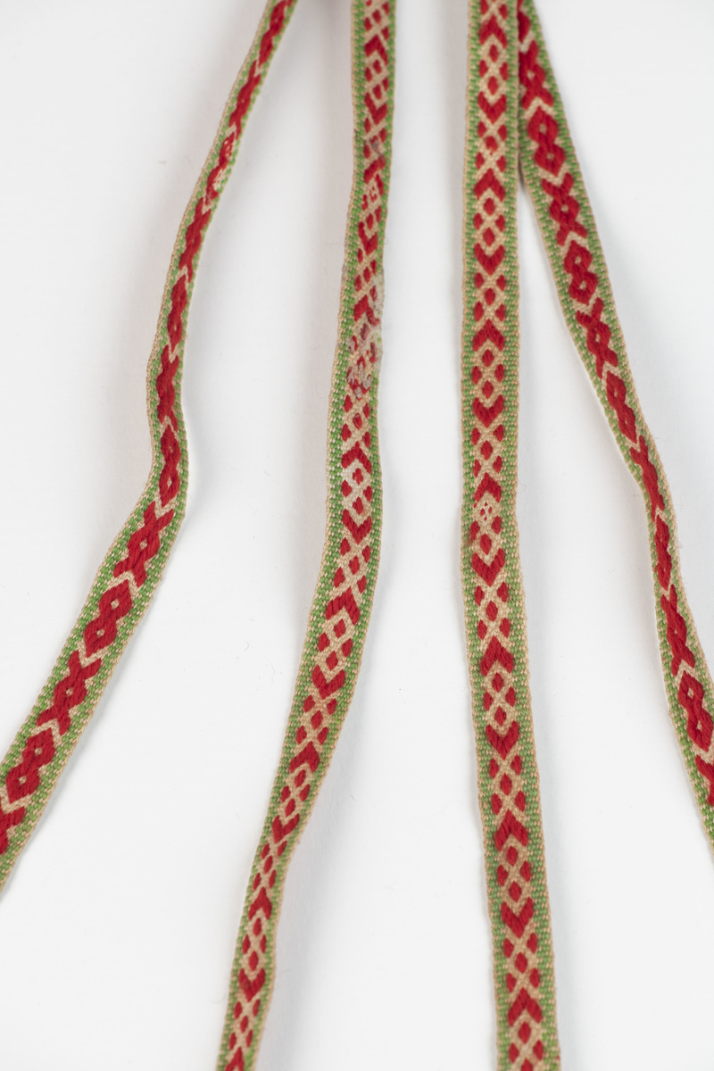 Et par hosebånd. Vevd av ulltråd, grønne kanter og geometrisk motiv i rødt og hvitt. Ulldusker i grønt, rødt og hvitt i endene. 