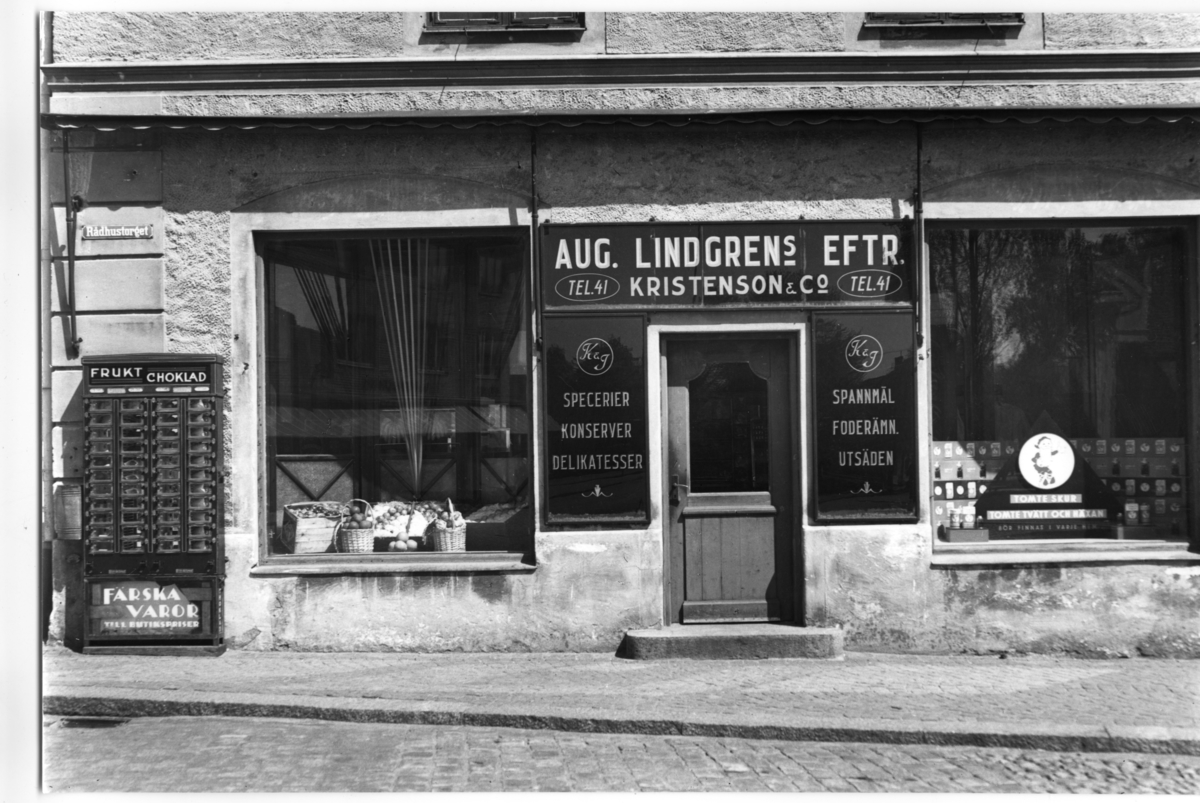 Magasinet, som uppfördes av korsvirke 1862 (brf), har bl a. inrymt en "Förvaringsbod för Mekanisk Brandstege" 1917-1928 och sistnämnda år inretts till två butiker i bottenvåningen. (Stig Pärson)  Butiken på bilden är AUG. LINDGRENs EFTR.  KRISTENSON & Co.
