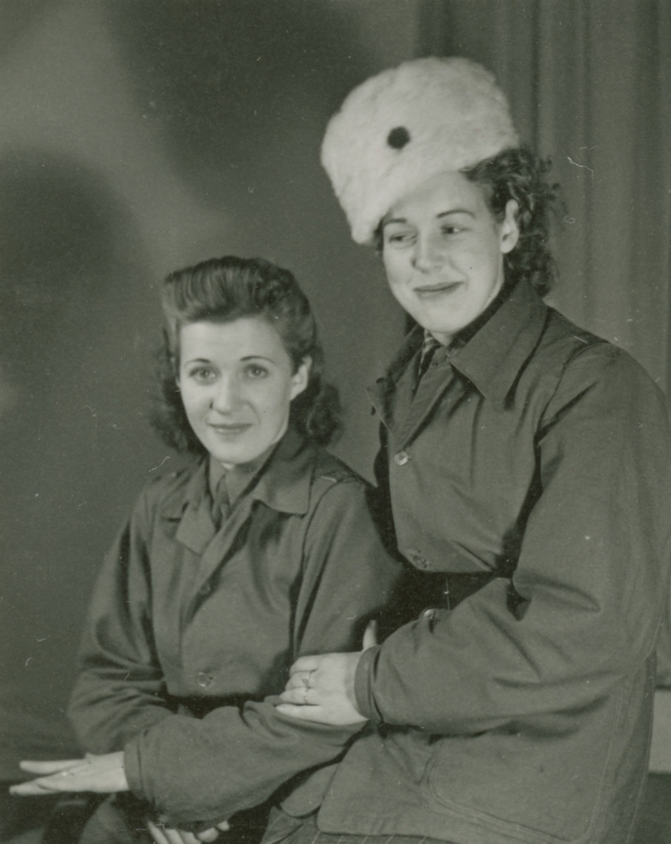 Porträttfoto av två frivilliga luftbevakare ur 91:a ls-kompaniet, stationerade i Tellejåkk, Kåbdalis under beredskapen, 1942. Klädda i uniform. Till vänster Karin Olsson, till höger Karin Nordberg. Klädda i militäruniform.
Serie om två bilder.