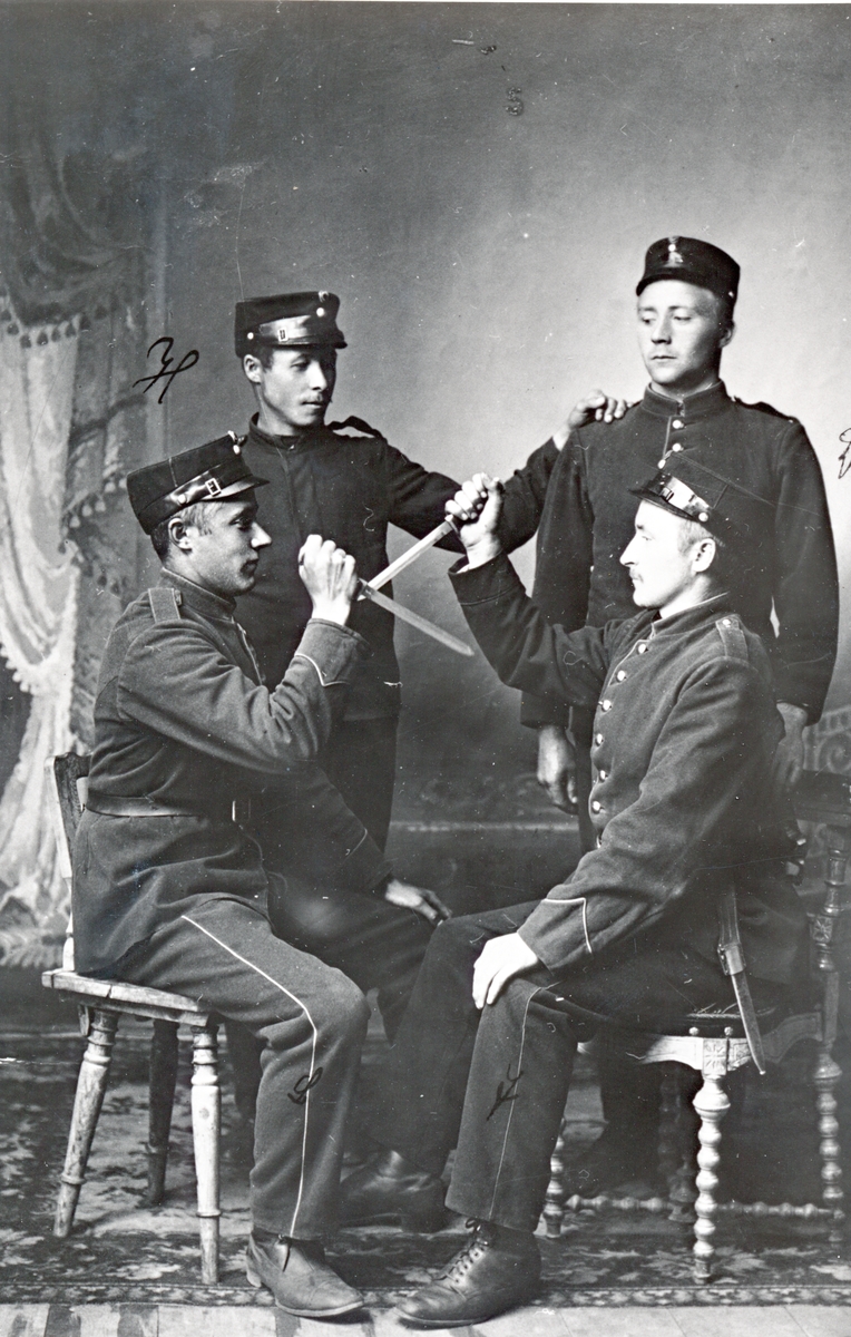 Atelierportrett av fire menn i militæruniform. De to foran trekker dolk. Ca. 1920.