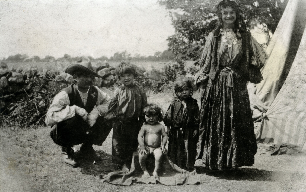 Romsk familj utanför sitt tält i Kalmar 1924. Fotografiet har inlämnats till Kalmar länsmuseum tillsammans med uppgiften att familjen på bilden fått stanna längre på platsen än de föreskrivna två veckorna eftersom mannen fått blodförgiftning i händerna. På bilden syns mannen med bandagerade händer. Övriga romska familjer avvisades.
