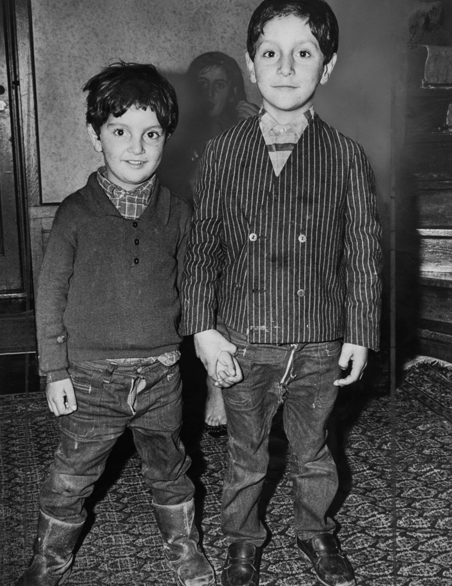 Två romska pojkar står leende på en mönstrad matta.