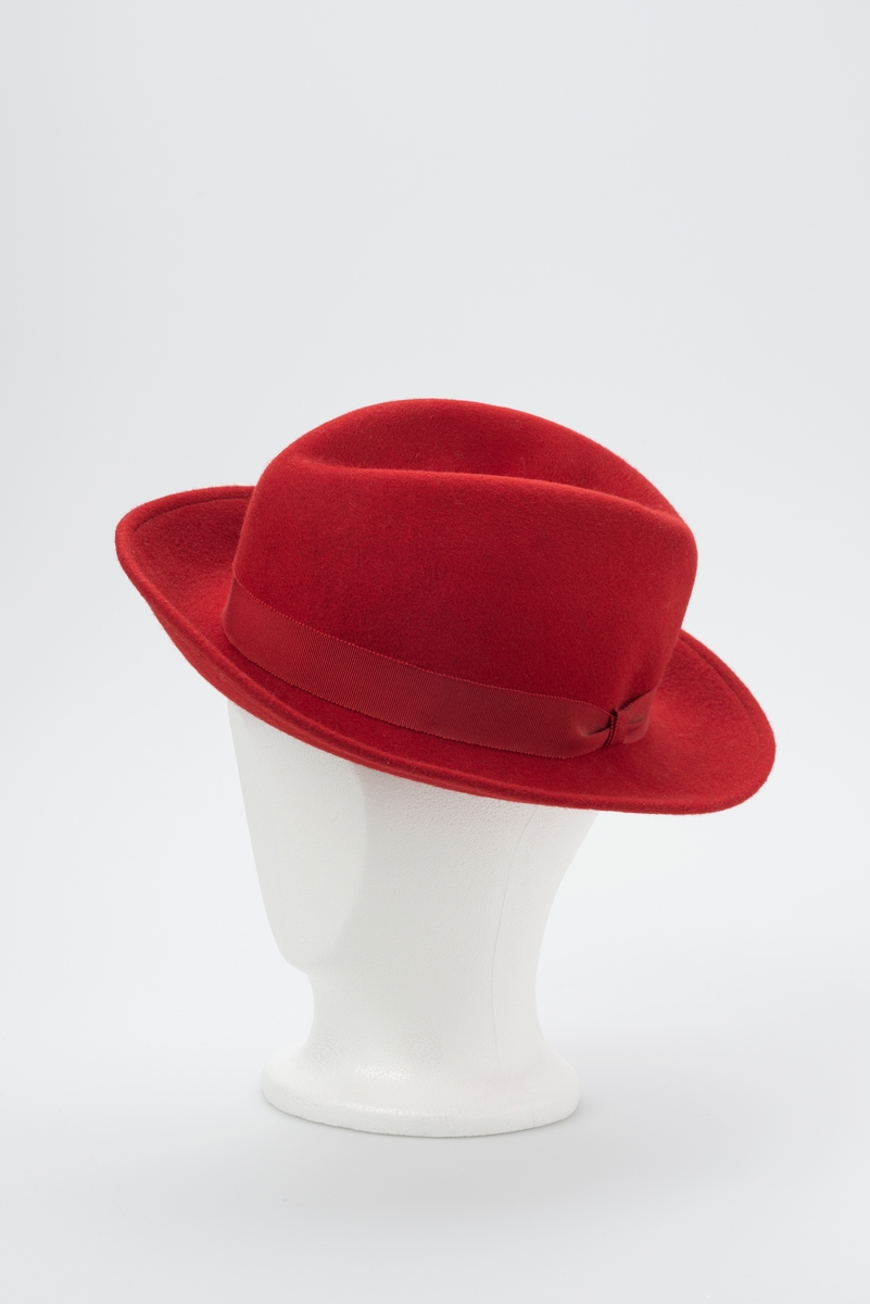Rød hatt med herrehattfasong. Vevd dekorbånd rundt pull.