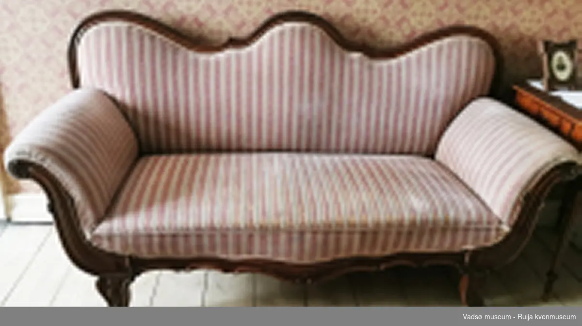 Rektangulær sofa i Biedermeier-stil. S-formet ryggbrett. Glatt, profilert rygglist. S-formede utoversvungne lener og lett utoversvungne bein. Lener, nedre kant av sargen og sofabeina er dekorert med utskåret blad-/knoppedekor. Sofaen er stoppet og er trukket i rosa, hvitstripet stoff.