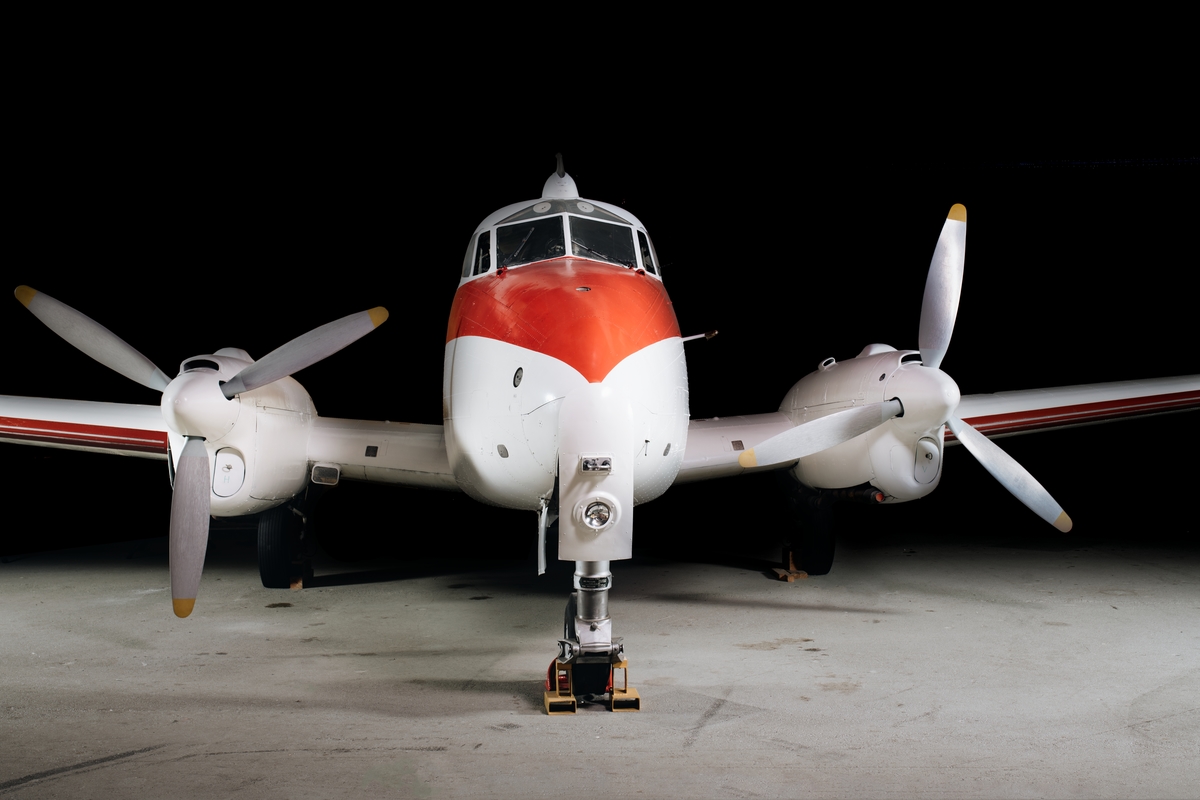 Flygplan av modell DH 104 Dove. Tvåmotorigt, lågvingat propellerflygplan av lättmetall. Vitmålat med röd registrering och dekor. Påskrift ”Triumph”.