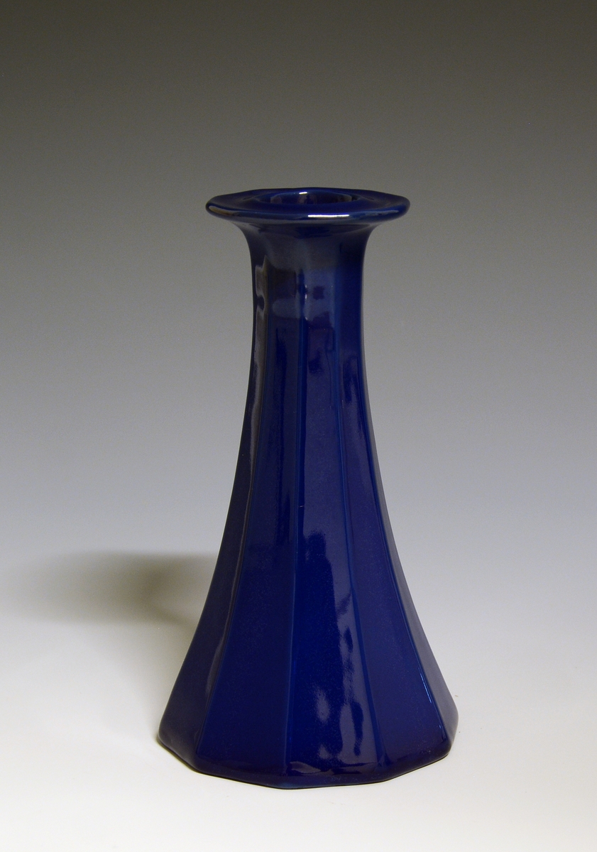 Mangekantet lysestake av porselen med blå glasur.
Modell: Octavia, tegnet av Grete Rønning i 1977
Dekor: Blå glasur