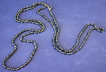 Runda pärlor av svart sten, slipade till att få en kantig yta, trädda på tråd. Mellan varje pärla har tråden en knut.