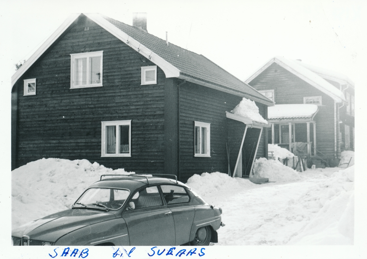 To 2 etasjers bolighus i tømmer. Bil av merke Saab parkert utenfor fremste huset.