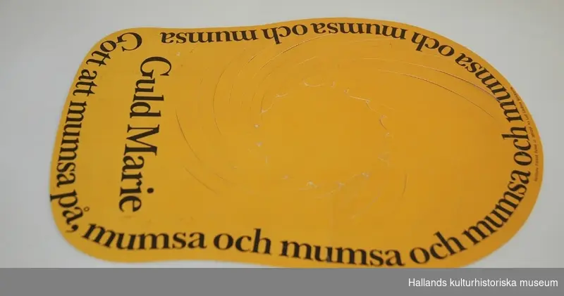 Kartongskiva genomstansad med spiralmönster vilket låter en kulle bildas, då mössan sättes på huvudet. Gul med svart reklamtext: "Guld Marie" "Gott att mumsa på". I mindre bokstäver: "Satatuote Finland Patent nr. 36912/67AB Leif Lindfors, Stockholm".