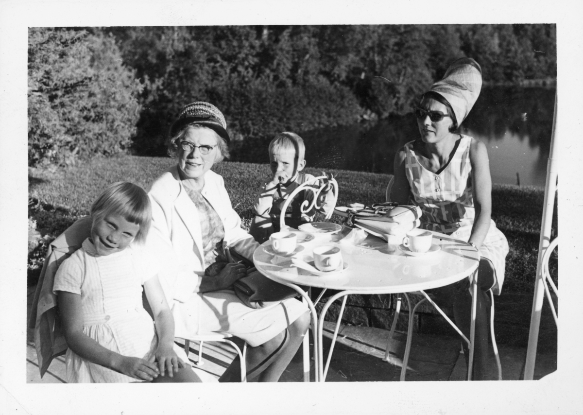 Kaffeslaberas i hagen med Ragnhild Omberg, datter og barnebarn. Fra venstre: Marianne Omberg Hyggen, Ragnhild Omberg, Kristoffer Omberg Hyggen og Else Solveig Omberg Hyggen, mor til barna. Trolig 1960-tall.