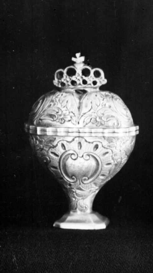 Svampehus av sølv, med hengslet lokk. Svampehuset har hjerteform med sokkel nederst, og en gjennombrutt krone øverst. Svampehuset har siselert dekor av blomsterslynger og barokkskjold.