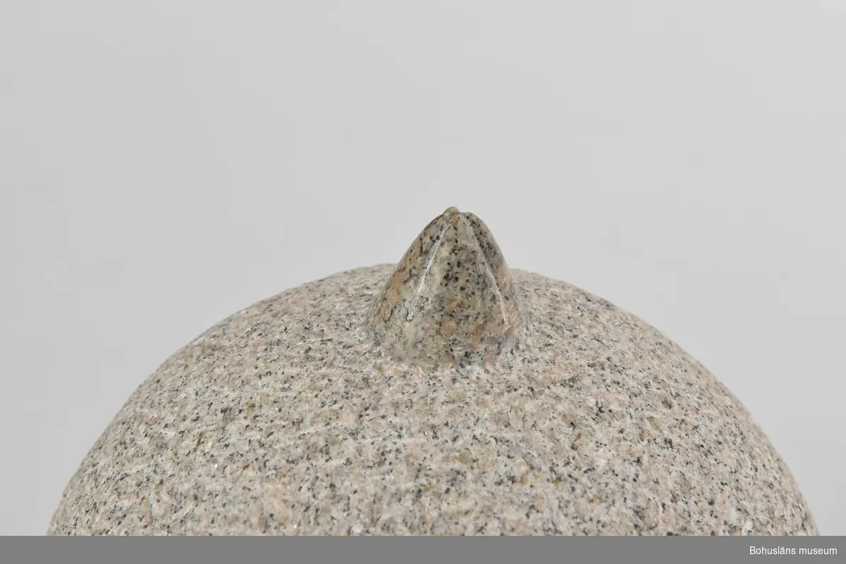 Runt klot av huggen granit med prickhuggen yta. Överst formen av en utsparad och slipad havstulpan. Monterad på en sockel med pyramdformad övre del.
Konstverk till  utmärkelsen "Bohuslän tackar" 1996.