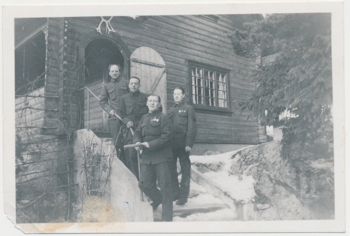 4 voksne menn i militæruniform foran hytta til Lars og Olga Mørk på Langebåt, ukjente