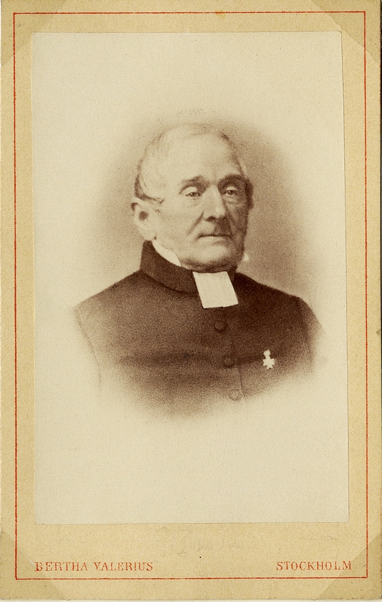 Porträttfoto av en äldre man i prästdräkt m.m. På bröstet skymtar en orden. 
Bröstbild, halvprofil. Ateljéfoto.