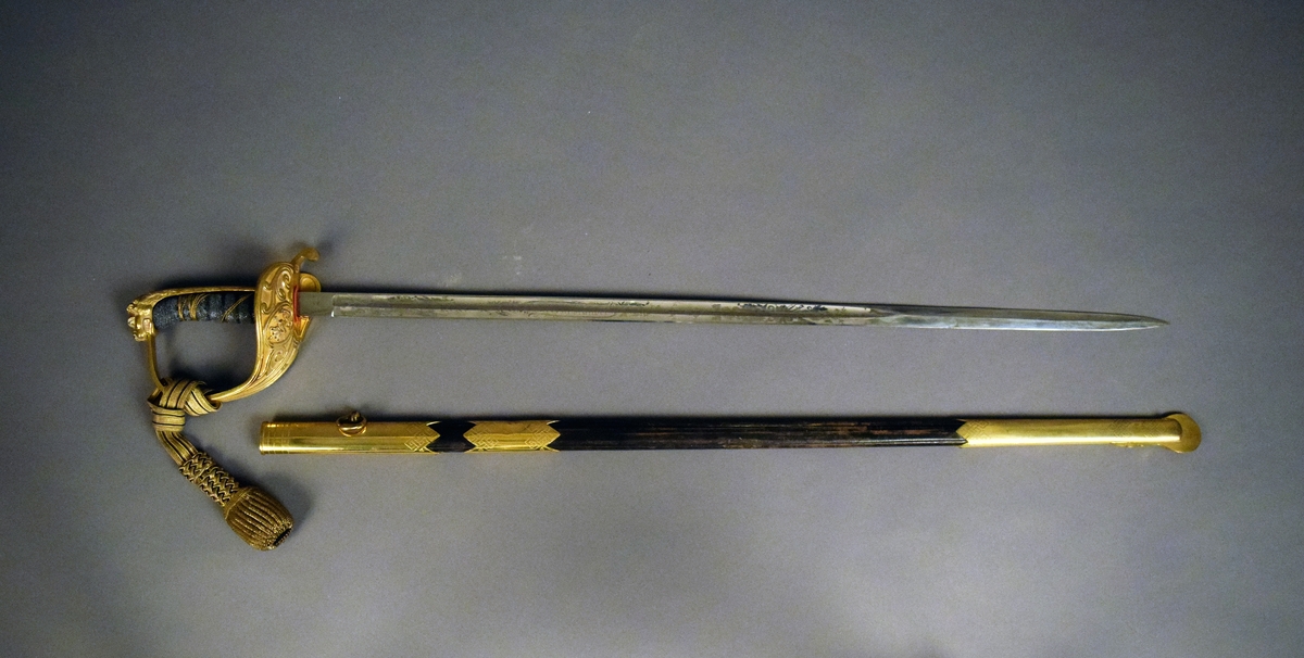 Sabel m/1915 med rak, ornamenterad klinga. Förgyllt handtag och parerskydd.