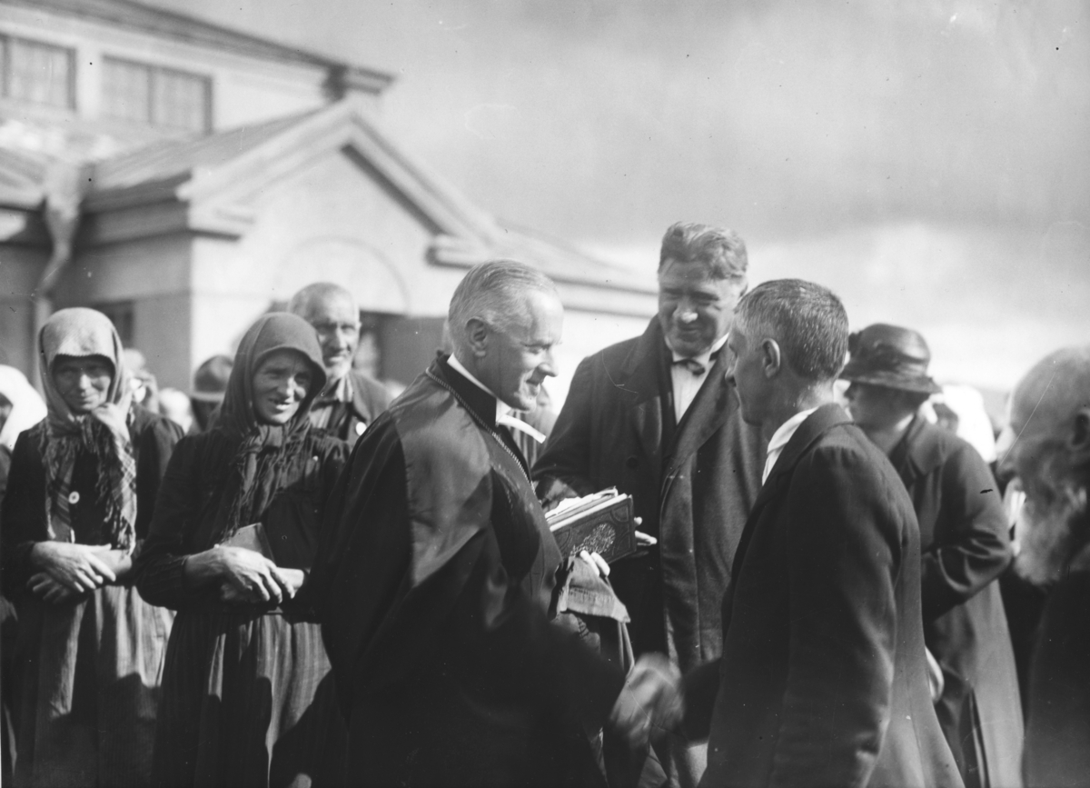 Nyanlända Svenskbybor på Ryhovs kasernområde i Jönköping 1929. Pastor Kristoffer Hoas (i mitten av bilden) presenterar skolläraren och klockaren (till höger) för biskop Edgar Reuterskjöld. I bakgrunden syns regementets matsalsbyggnad.