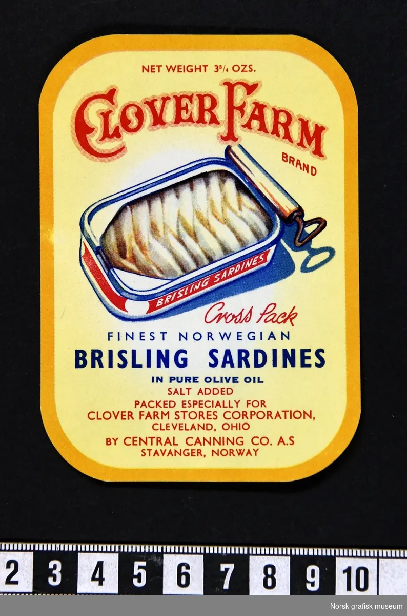 Gul etikett med mørkere gul bord. Tekst i rødt og blått, og midt på en fremstilling av en åpnet hermetikkboks med sardiner. 

"Finest Norwegian brisling sardines in pure olive oil"
