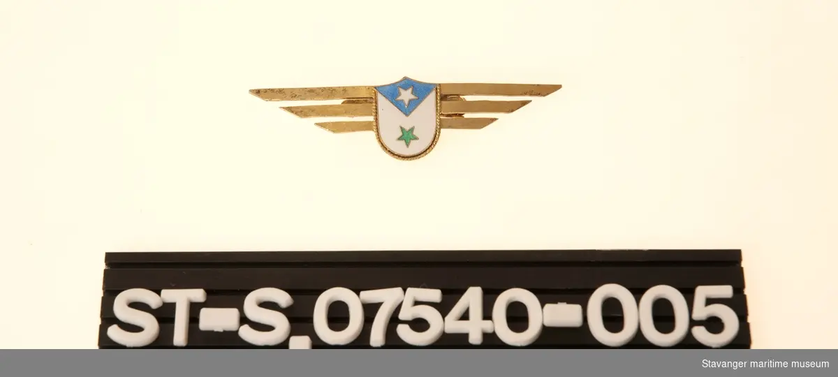 Luemerke til kvinne uniform. Gullfarget metall med farget logo i midten.