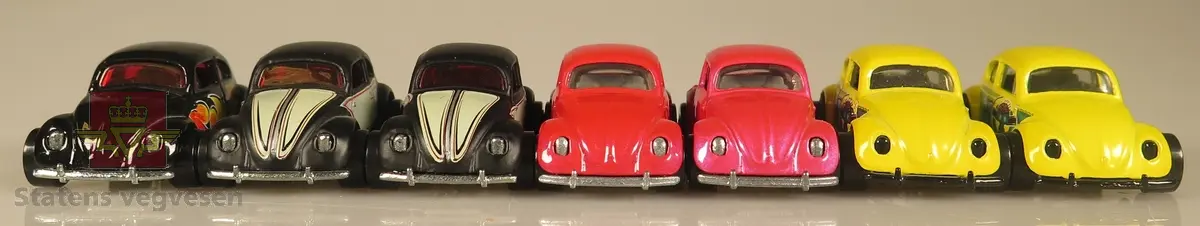 Samling av flere modellbiler. 2 biler er gule, 2 biler er røde, 2 biler er svarte med hvite dekaler og 1 bil er svart med flammedekaler. Alle er laget av metall og har en skala på 1:64